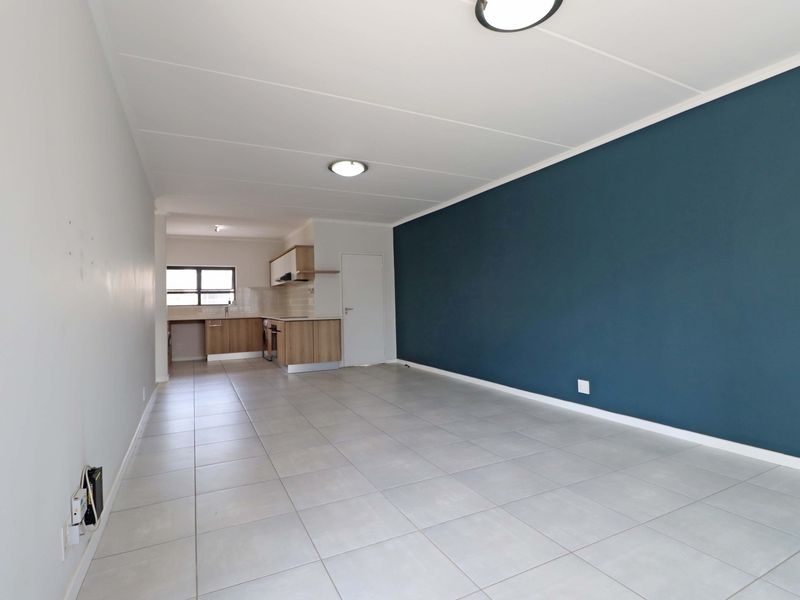 An open-plan living and kitchen area featuring neutral tiled flooring, a modern blue accent wall, and functional built-in kitchen cabinetry with integrated appliances.