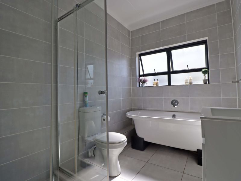 Modern bathroom featuring a freestanding bathtub, glass-enclosed shower, toilet, and vanity with neutral grey wall and floor tiling.