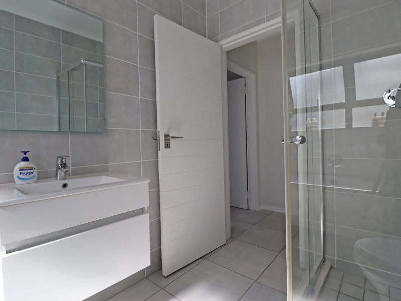 Modern bathroom featuring a wall-mounted vanity, basin, and a glass-enclosed shower with neutral grey wall and floor tiling.