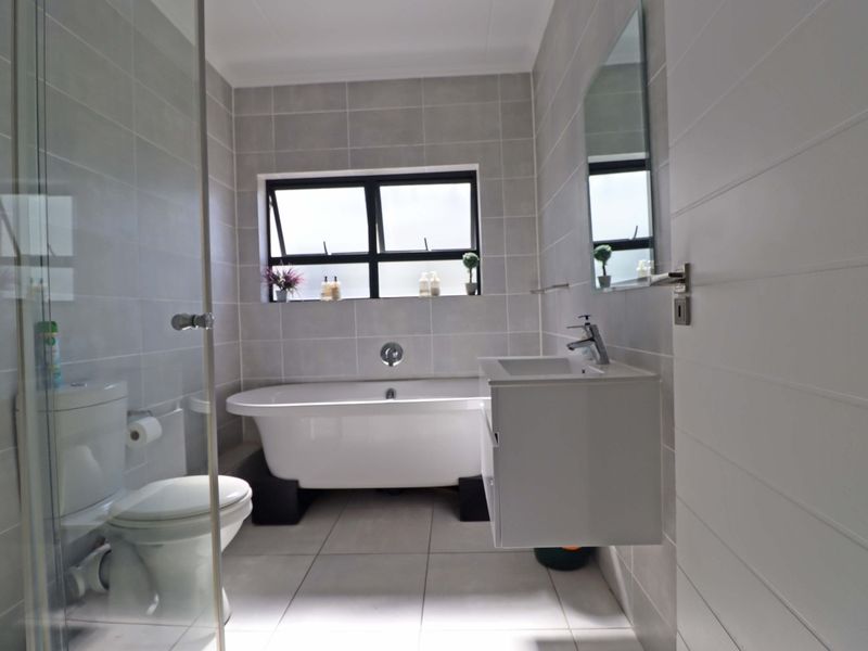 Modern bathroom featuring a freestanding bathtub, glass-enclosed shower, wall-mounted vanity, and neutral grey tiling throughout.