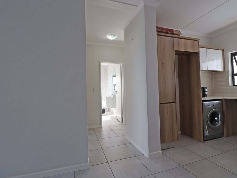 Open plan area featuring tiled flooring, built-in kitchen cabinetry with laundry plumbing, and a clear view through to the bathroom.