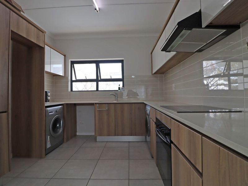 Modern kitchen featuring wood-finish cabinetry, stone countertops, subway tile backsplash, and integrated appliances including an oven, hob, and extractor fan.