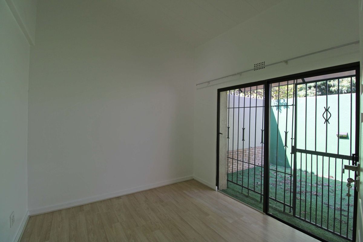 An empty bedroom featuring light-toned laminate flooring and a sliding glass door with a security gate, providing direct access to a private outdoor area.