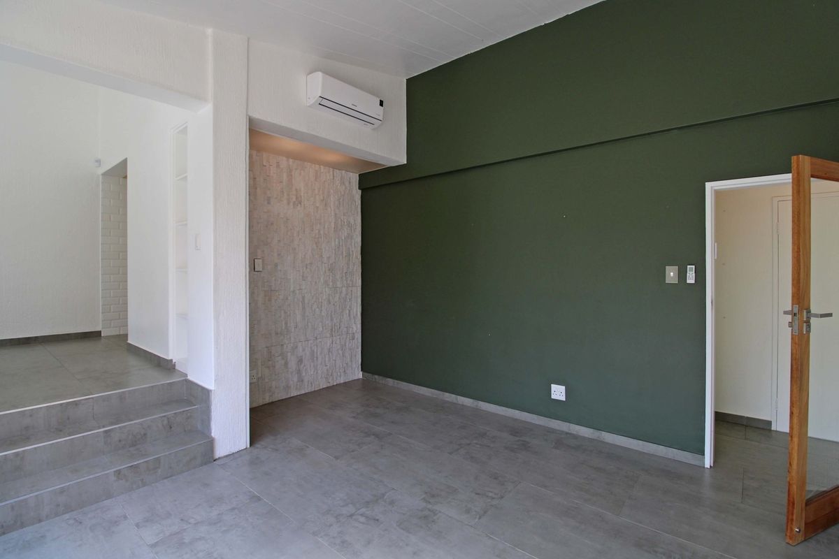An empty living area featuring modern grey floor tiles, a striking dark green accent wall, a stone feature wall, and a wall-mounted air conditioning unit.