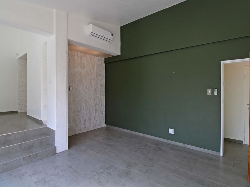 An empty living area featuring modern grey floor tiles, a striking dark green accent wall, a stone feature wall, and a wall-mounted air conditioning unit.