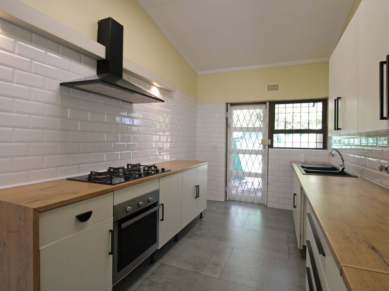 Modern kitchen featuring subway tile backsplash, wooden countertops, gas hob, built-in oven, and direct access to the exterior via a security gate.