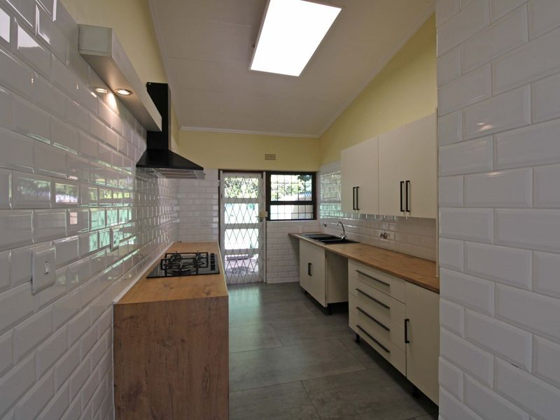 A clean, modern galley-style kitchen featuring white subway tile backsplashes, wooden countertops, built-in cabinetry, and a gas hob with an extractor fan.