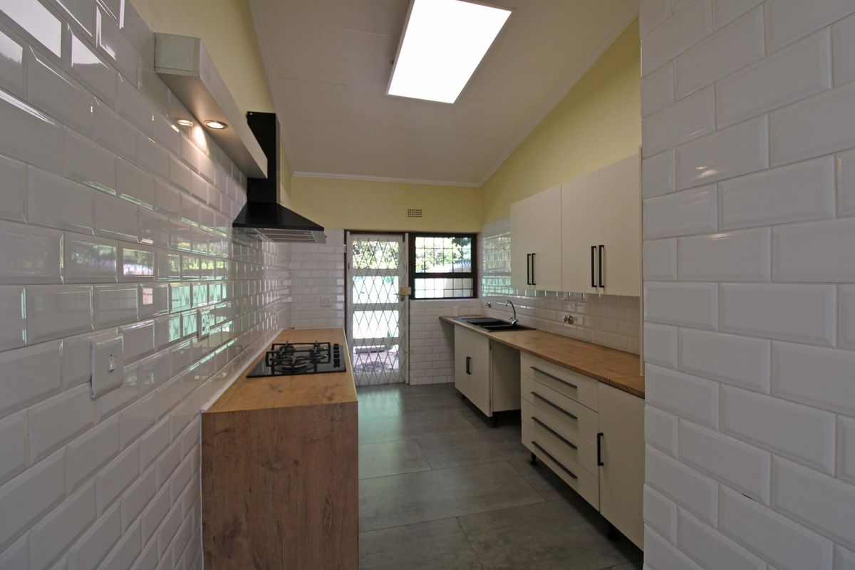 A clean, modern galley-style kitchen featuring white subway tile backsplashes, wooden countertops, built-in cabinetry, and a gas hob with an extractor fan.