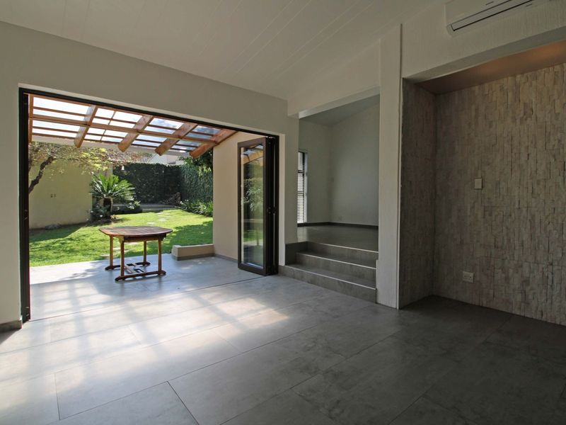 Spacious open-plan living area featuring large bi-fold doors opening to a covered patio, stone feature wall, and modern tiled flooring.