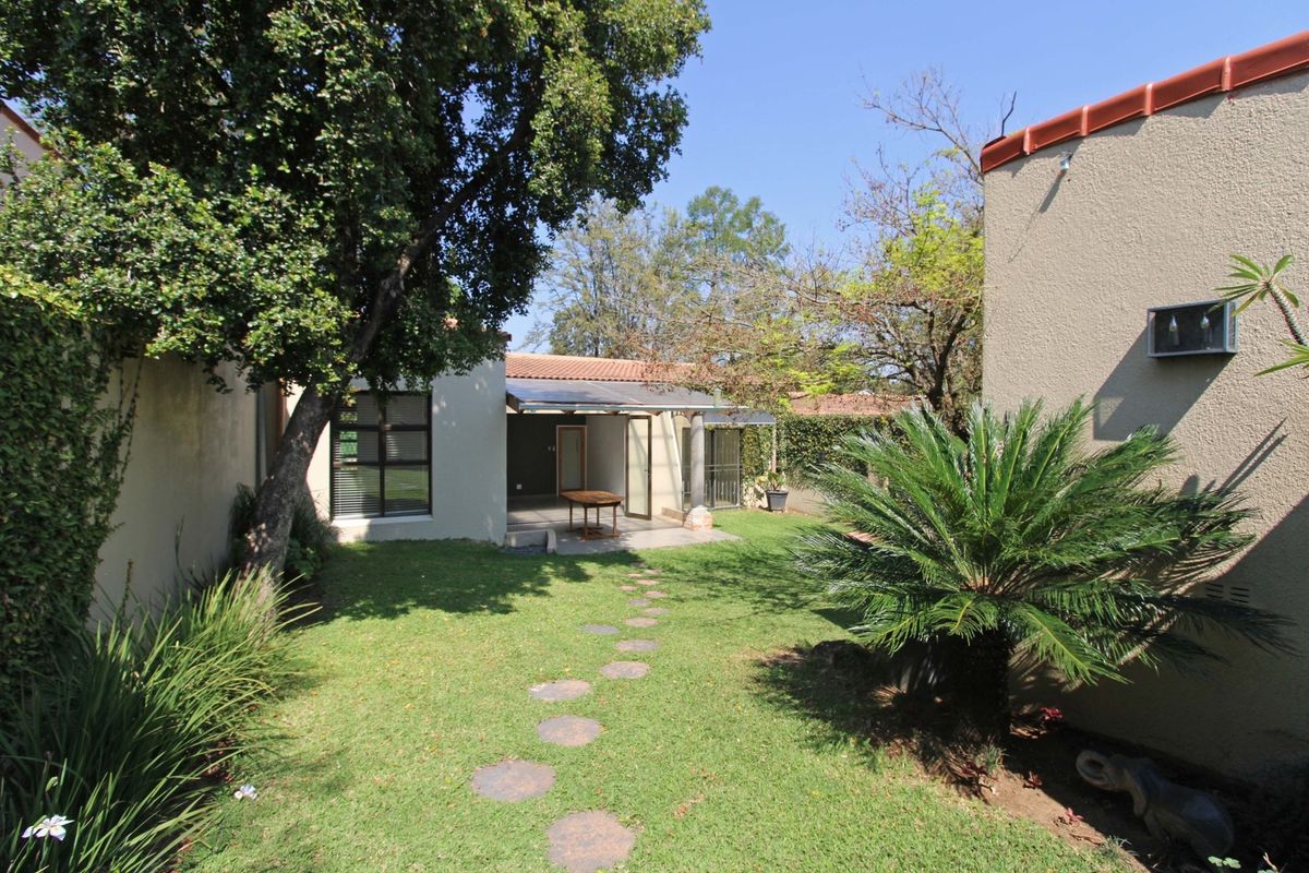 A private rear garden featuring a lawn, mature trees, a stepped stone path, and a covered patio area attached to the townhouse.