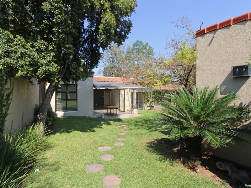 A private rear garden featuring a lawn, mature trees, a stepped stone path, and a covered patio area attached to the townhouse.