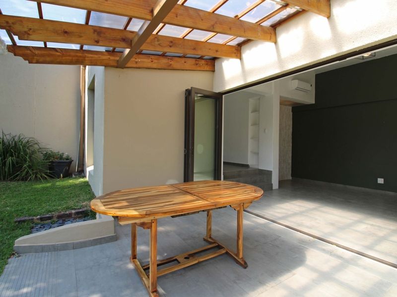Covered patio area featuring a timber pergola with translucent roofing, tiled floors, and seamless access to the interior through large stacking glass doors.