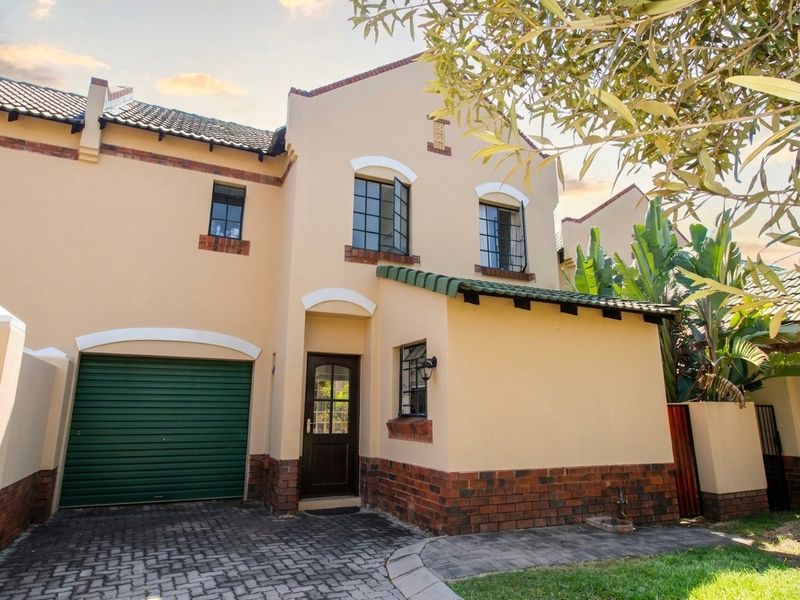 Front elevation of a townhouse featuring a single garage, paved driveway, and traditional brick and plaster facade with tiled roofing.