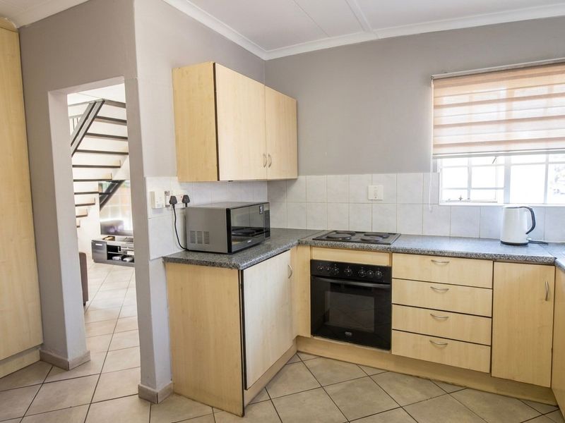 Functional kitchen featuring light wood cabinetry, laminate countertops, built-in oven, electric hob, and tiled flooring, with an adjacent view of the staircase.