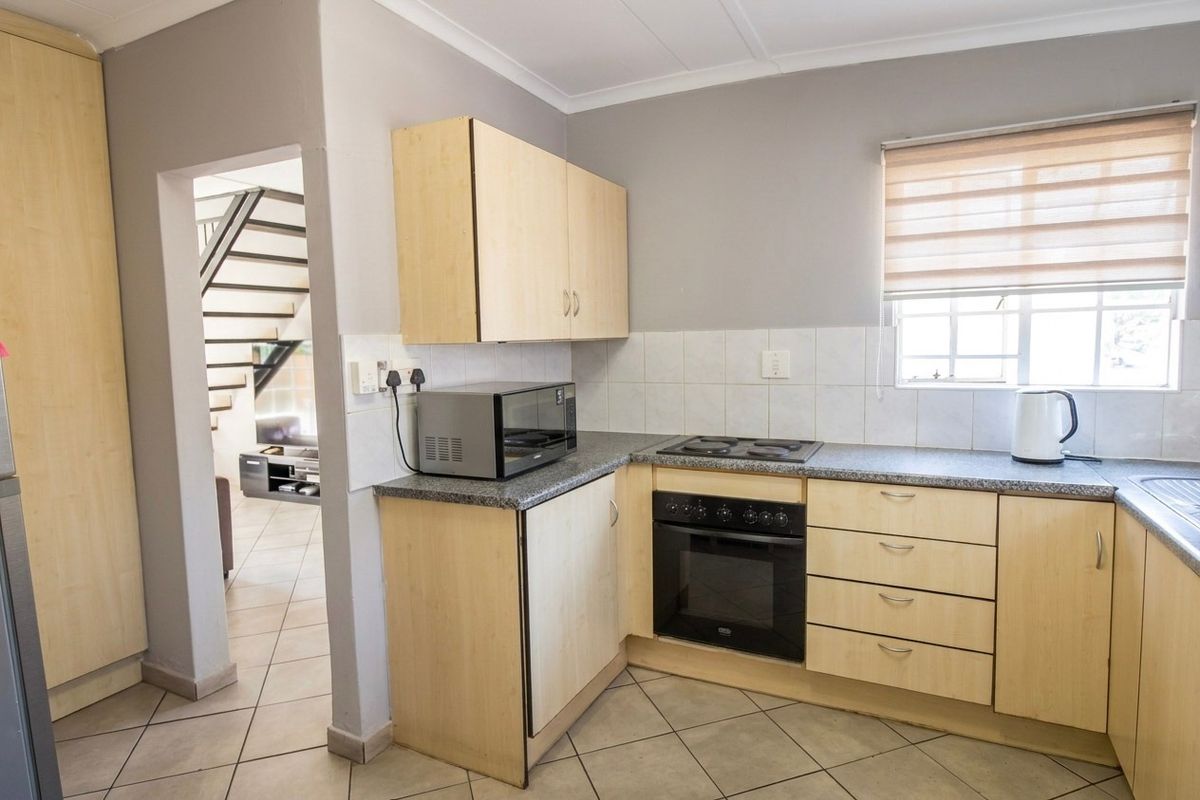 Functional kitchen featuring light wood cabinetry, laminate countertops, built-in oven, electric hob, and tiled flooring, with an adjacent view of the staircase.