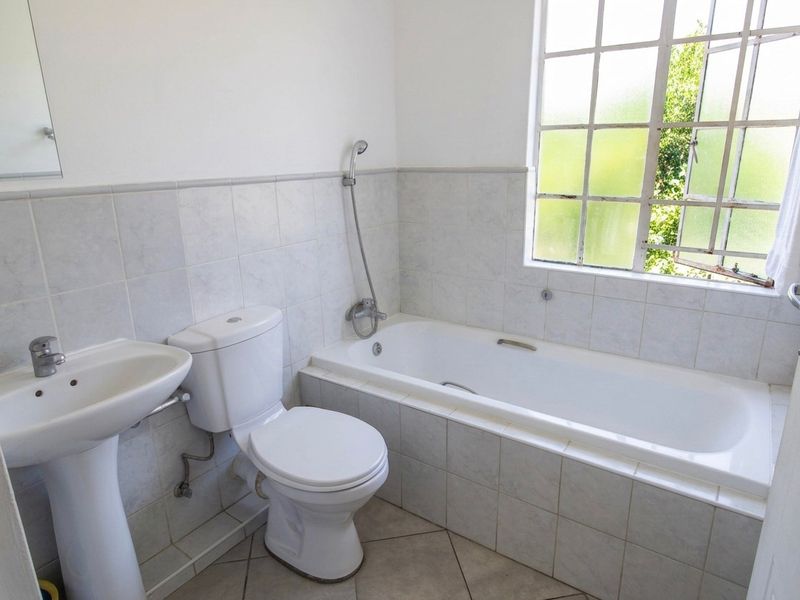 A functional bathroom featuring a pedestal basin, toilet, and a built-in bathtub with a handheld shower mixer, finished with neutral wall and floor tiles.