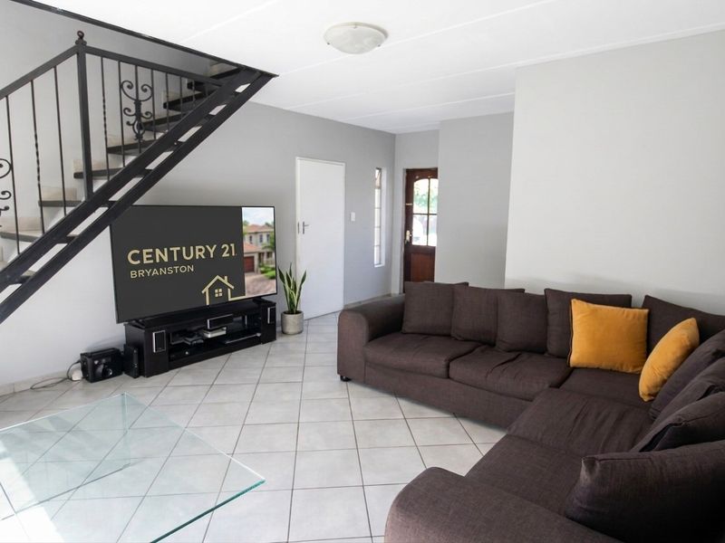 Open-plan living area featuring ceramic floor tiles and a wrought iron staircase leading to the upper level.