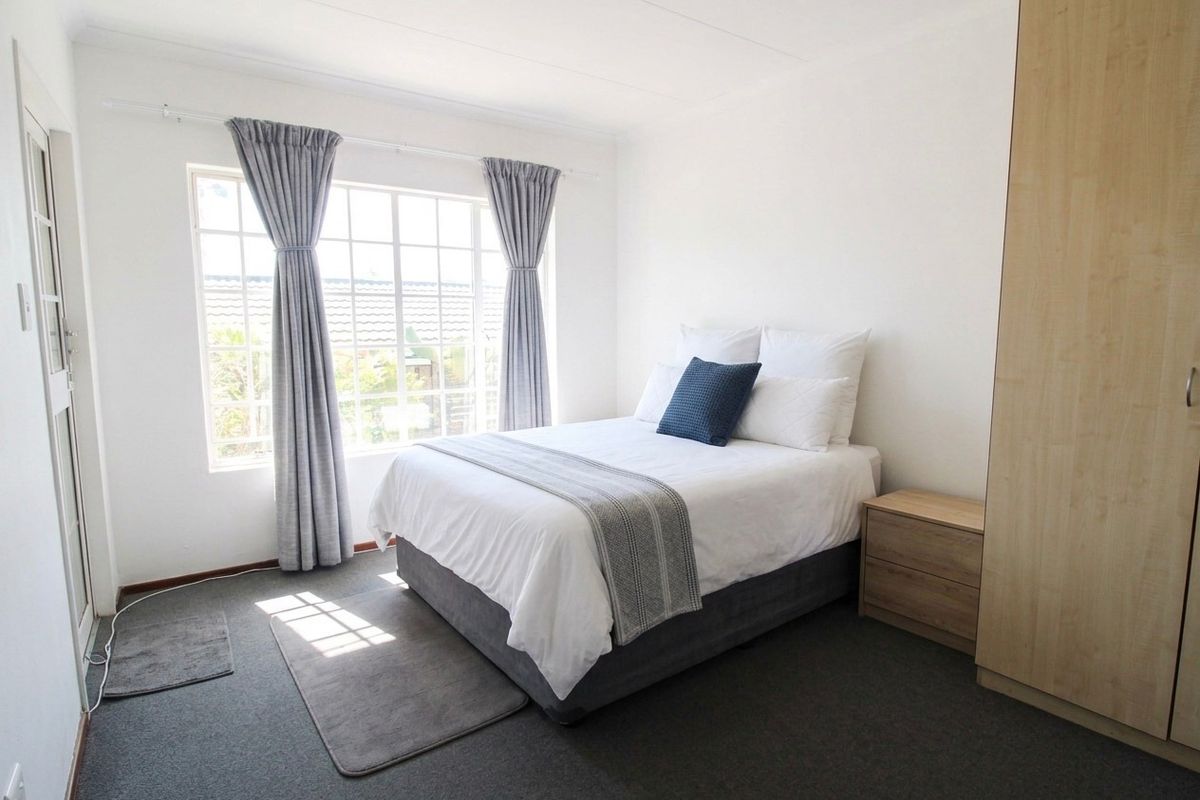 A bright and well-maintained bedroom featuring a built-in wardrobe, neutral carpeting, and a large grid-pattern window allowing for ample natural light.