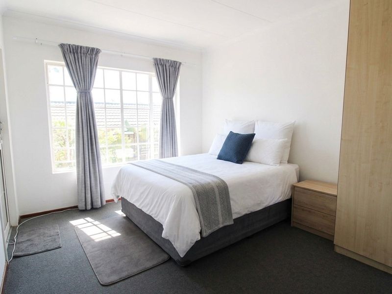 A bright and well-maintained bedroom featuring a built-in wardrobe, neutral carpeting, and a large grid-pattern window allowing for ample natural light.