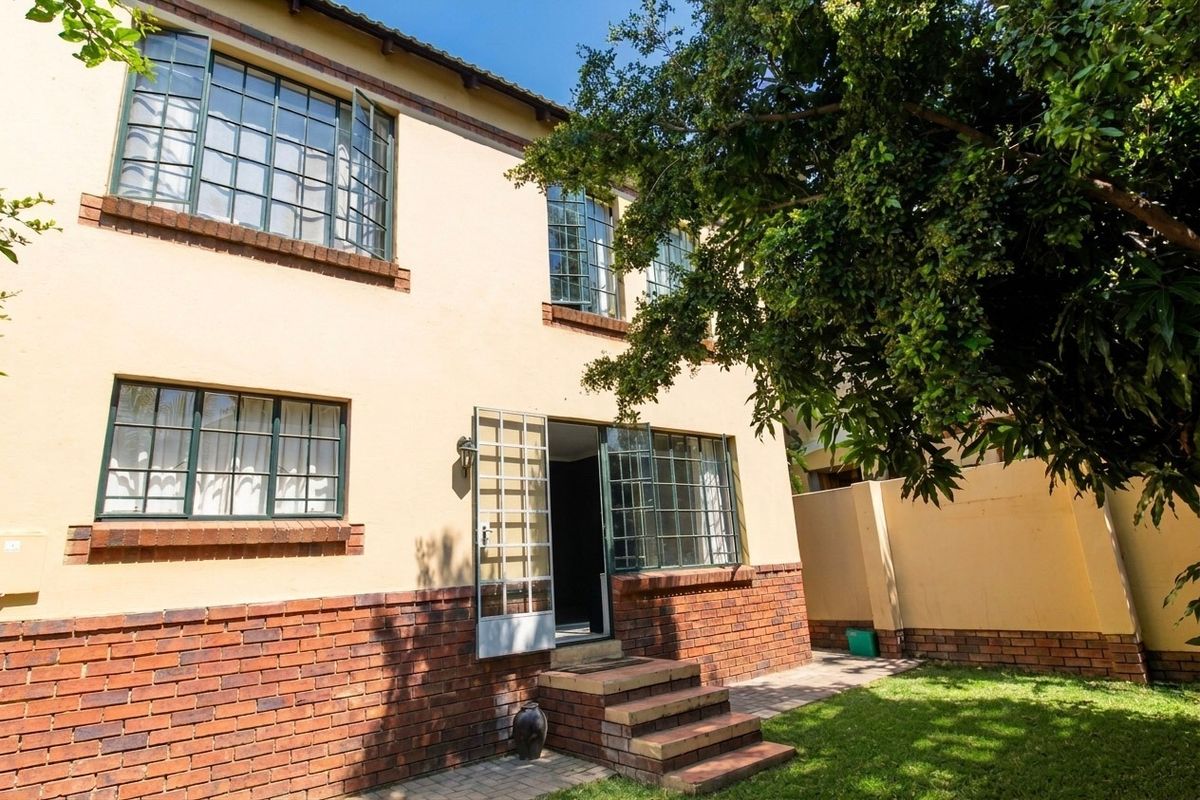 Rear view of a two-story townhouse featuring a brick and plaster facade, steel-framed windows, and a small garden area with brick steps.