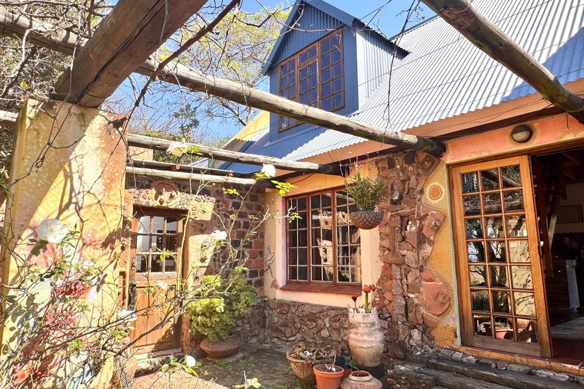 A rustic outdoor patio area featuring stone masonry walls, timber pergola structure, and traditional timber-framed windows and doors under a corrugated metal roof.