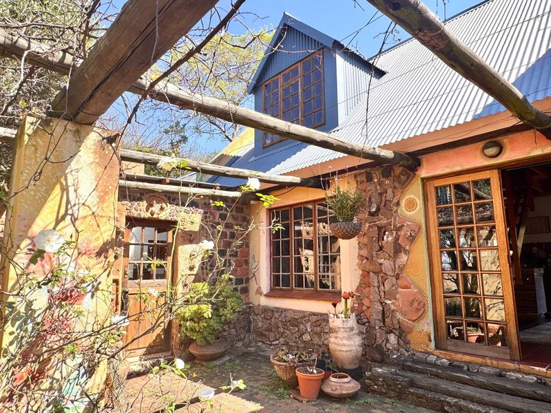 A rustic outdoor patio area featuring stone masonry walls, timber pergola structure, and traditional timber-framed windows and doors under a corrugated metal roof.