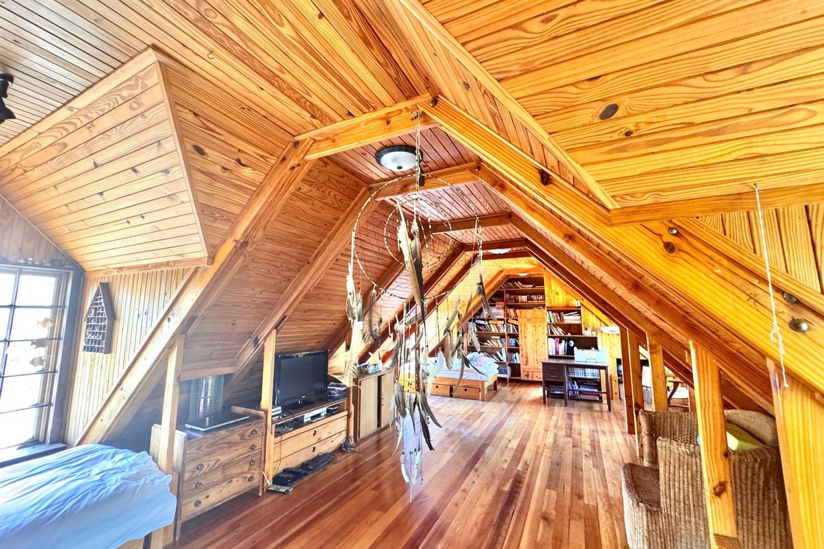 Spacious attic-style bedroom featuring extensive timber finishes, exposed rafters, hardwood flooring, and integrated built-in shelving units.