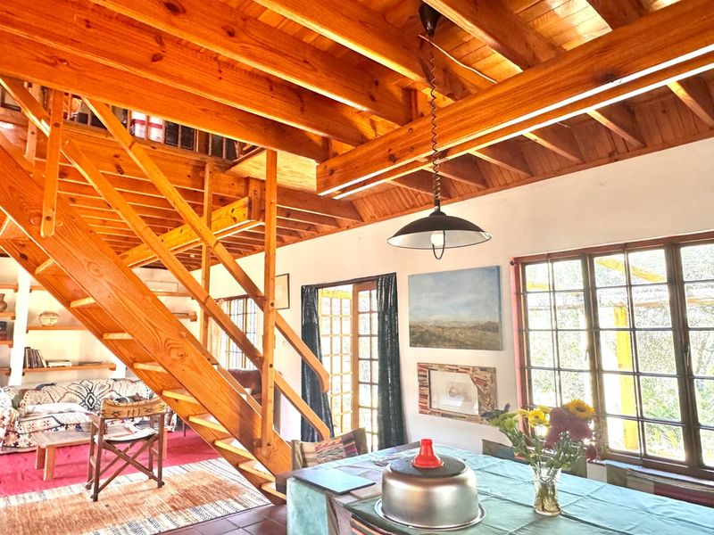 Open plan living area featuring exposed timber ceiling beams, a wooden staircase, and large timber-framed windows providing natural light.