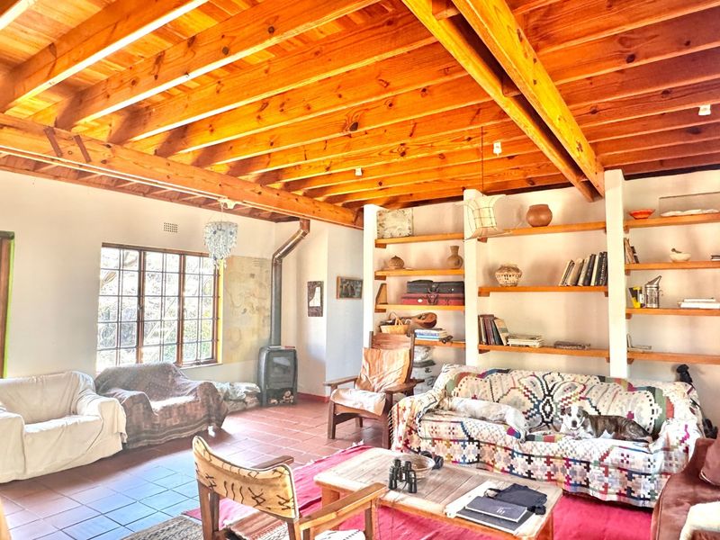 Spacious living room featuring a high exposed timber beam ceiling, built-in shelving units, a wood-burning fireplace, and classic tiled flooring.