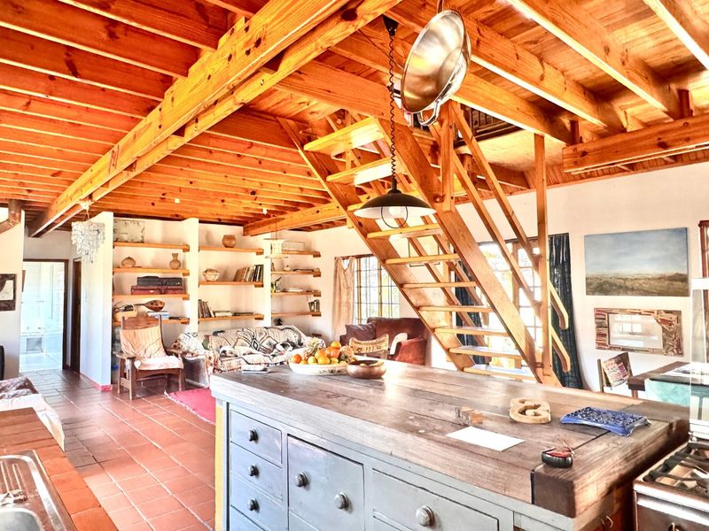 Spacious open-plan living area featuring exposed timber ceiling beams, a central kitchen island, and a wooden staircase leading to an upper level.