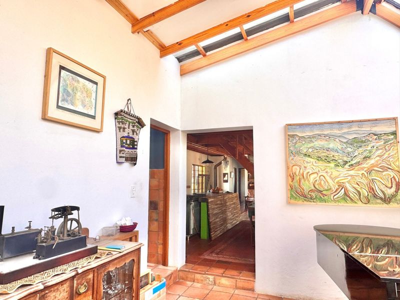 Living area featuring exposed timber roof beams, a skylight, and terracotta floor tiles, with a view through to the adjacent kitchen area.