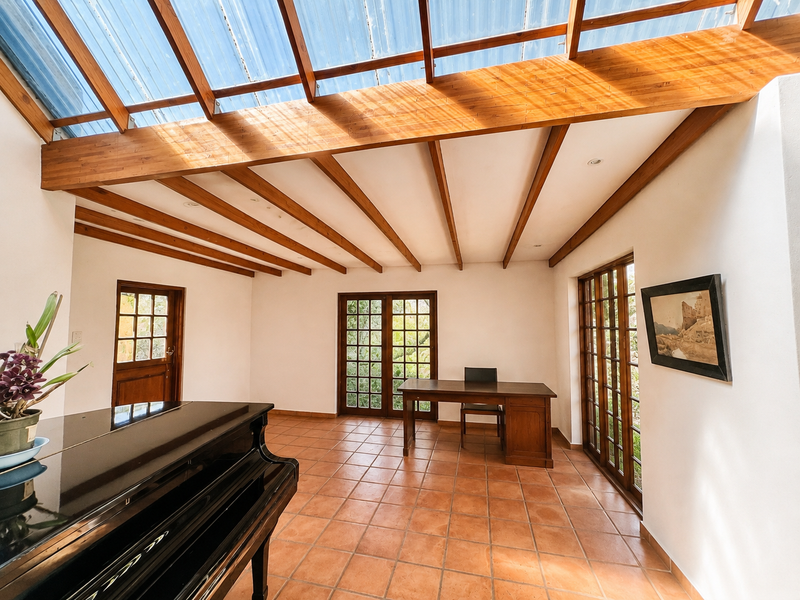 Spacious living area featuring exposed timber beams, a translucent roof for natural light, terracotta flooring, and multiple sets of french doors leading outdoors.