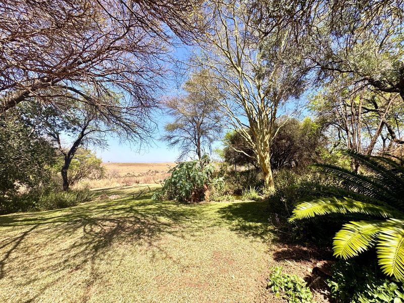 A peaceful, well-maintained garden area featuring mature trees and expansive lawn space with a scenic landscape view.