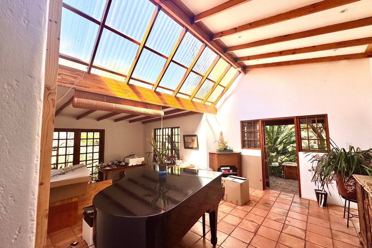 Spacious living area featuring a high pitched ceiling with exposed timber beams, a large corrugated skylight, and traditional terracotta floor tiles.