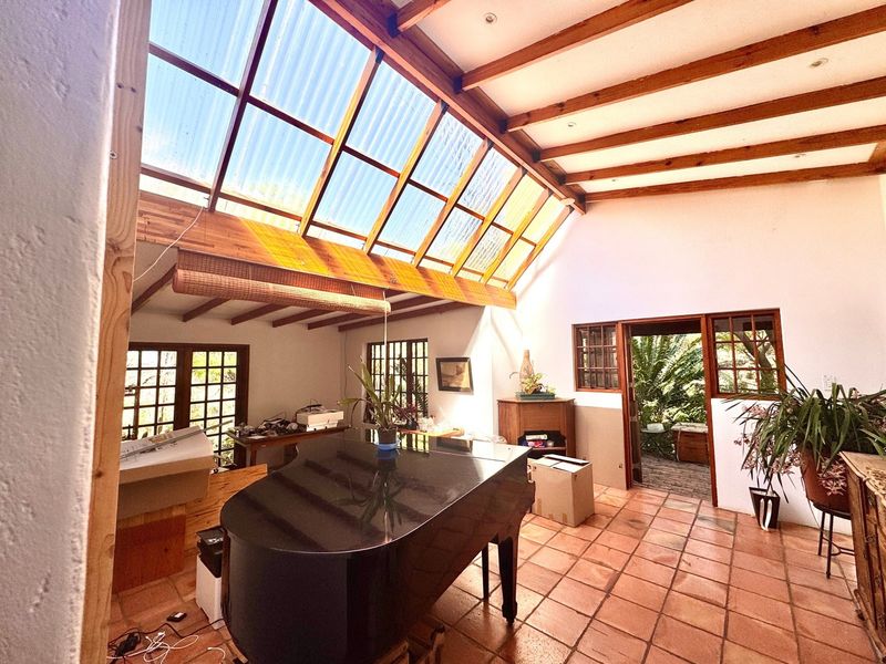Spacious living area featuring a high pitched ceiling with exposed timber beams, a large corrugated skylight, and traditional terracotta floor tiles.