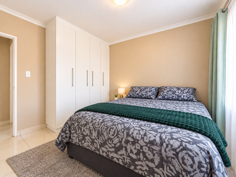 A well-maintained bedroom featuring neutral wall tones, tiled flooring, and a spacious white built-in wardrobe providing ample storage.
