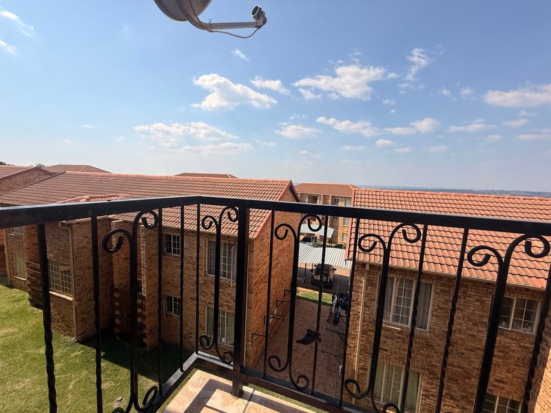 A private balcony featuring a wrought iron balustrade and tiled flooring, offering an elevated view over the apartment complex grounds.