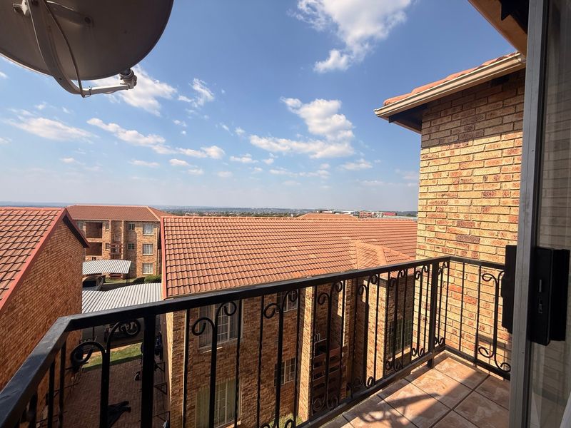 A private balcony featuring tiled flooring and a wrought iron railing, offering an elevated view of the surrounding apartment complex.