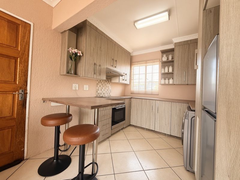 A functional kitchen featuring light wood-grain cabinetry, tiled flooring, a built-in oven and hob, and an integrated breakfast bar for casual dining.