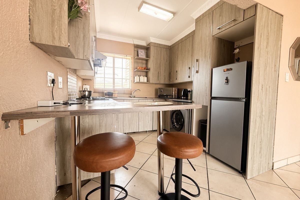 Compact kitchen featuring wood-look cabinetry, a breakfast bar, tiled flooring, and integrated appliances, offering a functional layout for daily meal preparation.