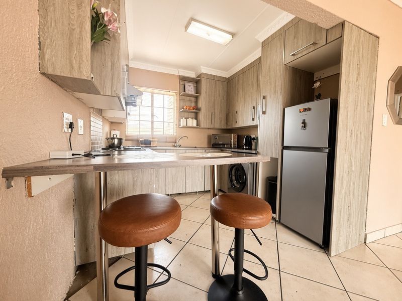 Compact kitchen featuring wood-look cabinetry, a breakfast bar, tiled flooring, and integrated appliances, offering a functional layout for daily meal preparation.