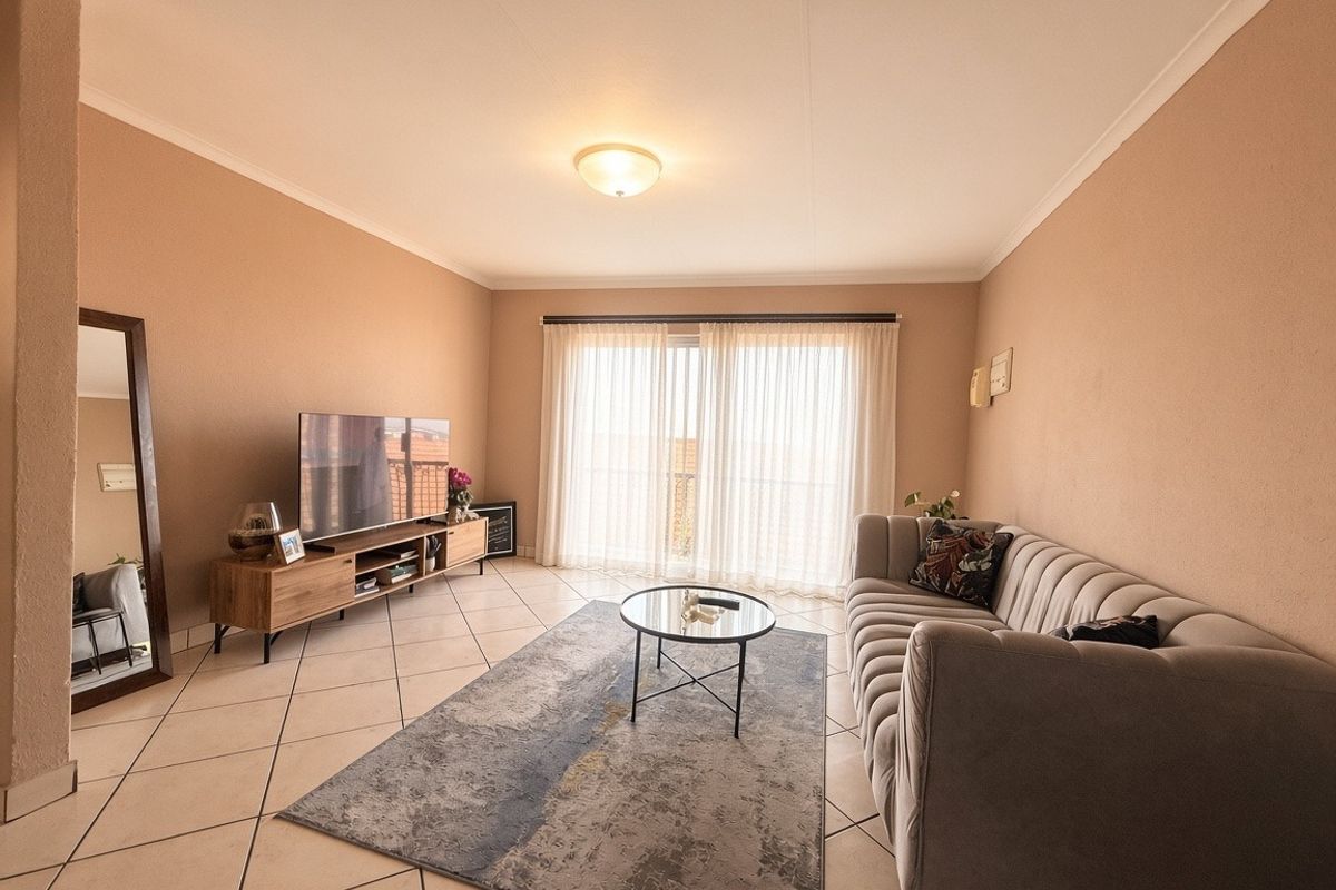 A well-maintained living room featuring neutral tiled flooring, a coved ceiling, and a large sliding glass door that provides ample natural light.