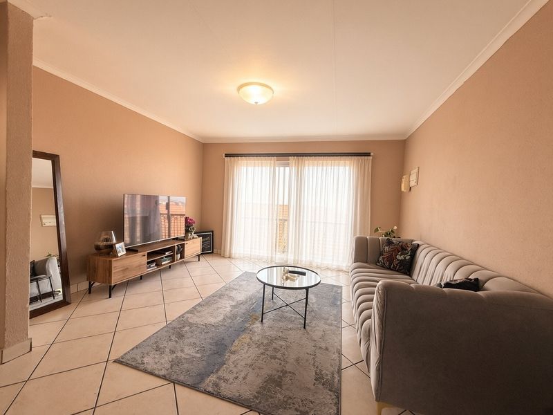 A well-maintained living room featuring neutral tiled flooring, a coved ceiling, and a large sliding glass door that provides ample natural light.