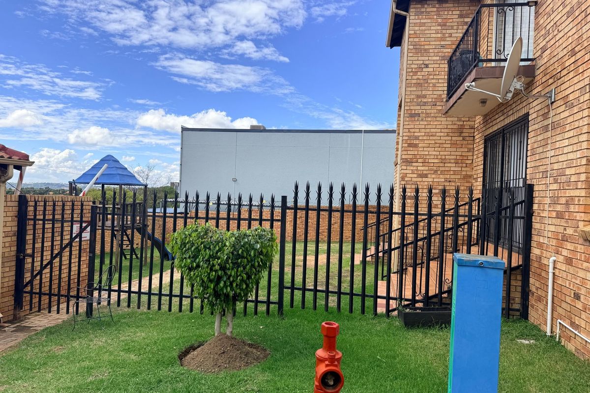 Rear view of a brick apartment building featuring a balcony with wrought iron railings and a secure fenced garden area.
