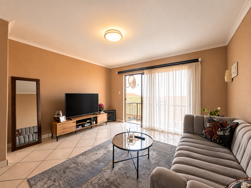 A well-maintained living room featuring tiled flooring, neutral wall tones, and a sliding glass door providing access to an outdoor balcony area.