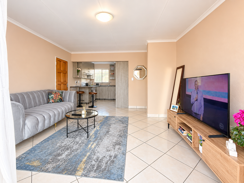 Open-plan living area featuring tiled flooring and a seamless transition to a functional kitchen with built-in cabinetry and a breakfast counter.