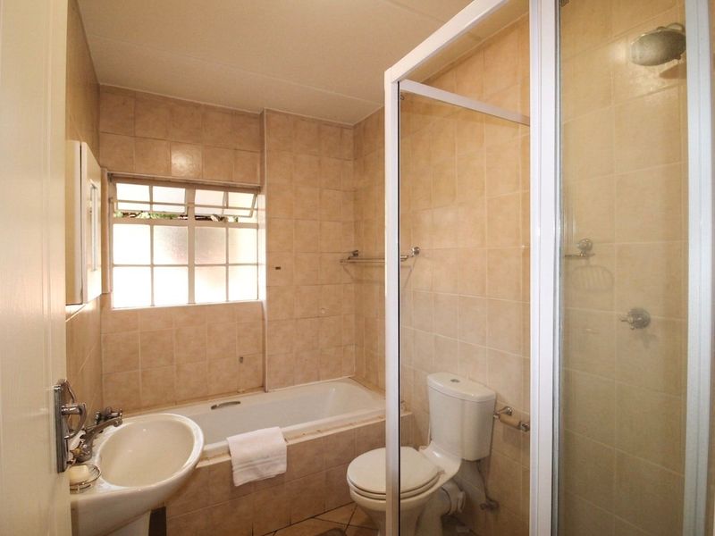 A functional bathroom featuring a bathtub, separate shower enclosure, pedestal basin, and toilet with neutral wall and floor tiling.