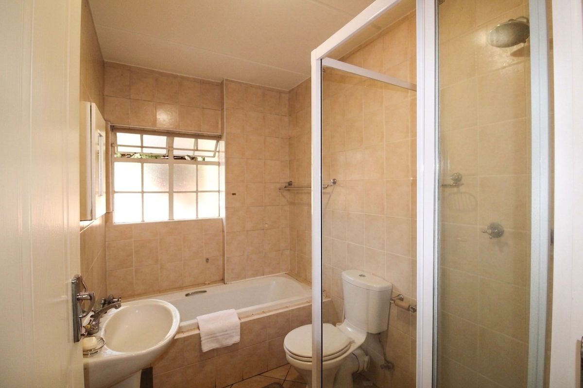 A functional bathroom featuring a bathtub, separate shower enclosure, pedestal basin, and toilet with neutral wall and floor tiling.