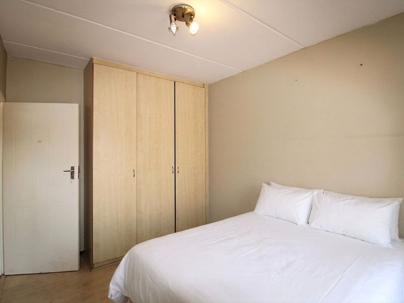 A functional bedroom featuring a built-in wooden wardrobe and neutral wall finishes, providing a clean and simple living space.