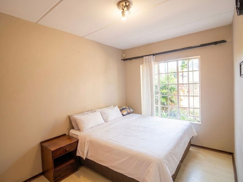 A functional bedroom featuring laminate flooring, a window with security bars, and a ceiling light fixture.